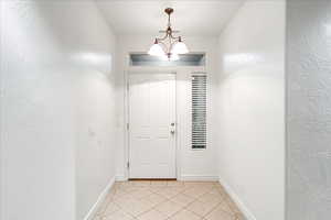 Entryway featuring tile patterned floors, a textured wall, and a chandelier