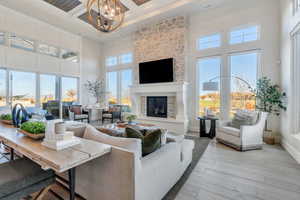 Living room featuring a towering ceiling, wood finished floors, a chandelier, a stone fireplace, and beamed ceiling