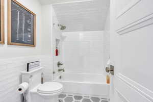 Full bath with shower / bath combination, tile walls, and a wainscoted wall