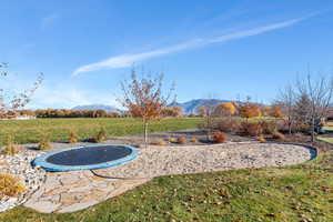 View of grassy yard with a trampoline and a mountain view