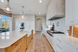 Kitchen with arched walkways, light wood-type flooring, recessed lighting, white cabinetry, and light stone counters