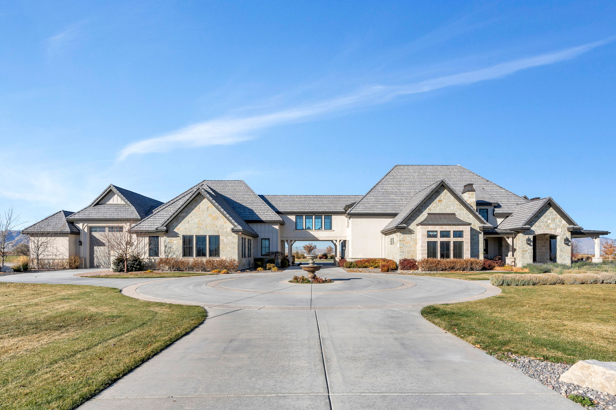 French provincial home featuring stone siding, a front lawn, and curved driveway