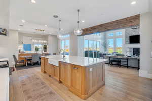 Kitchen with light wood finished floors, hanging light fixtures, a kitchen island with sink, open floor plan, and light stone countertops