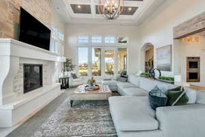 Living room featuring a towering ceiling, a premium fireplace, beamed ceiling, coffered ceiling, and a chandelier