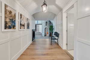 Hall featuring lofted ceiling, light wood-style floors, and a decorative wall