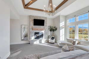 Primary bedroom featuring a raised ceiling, a stone fireplace, a towering ceiling, recessed lighting, and a chandelier