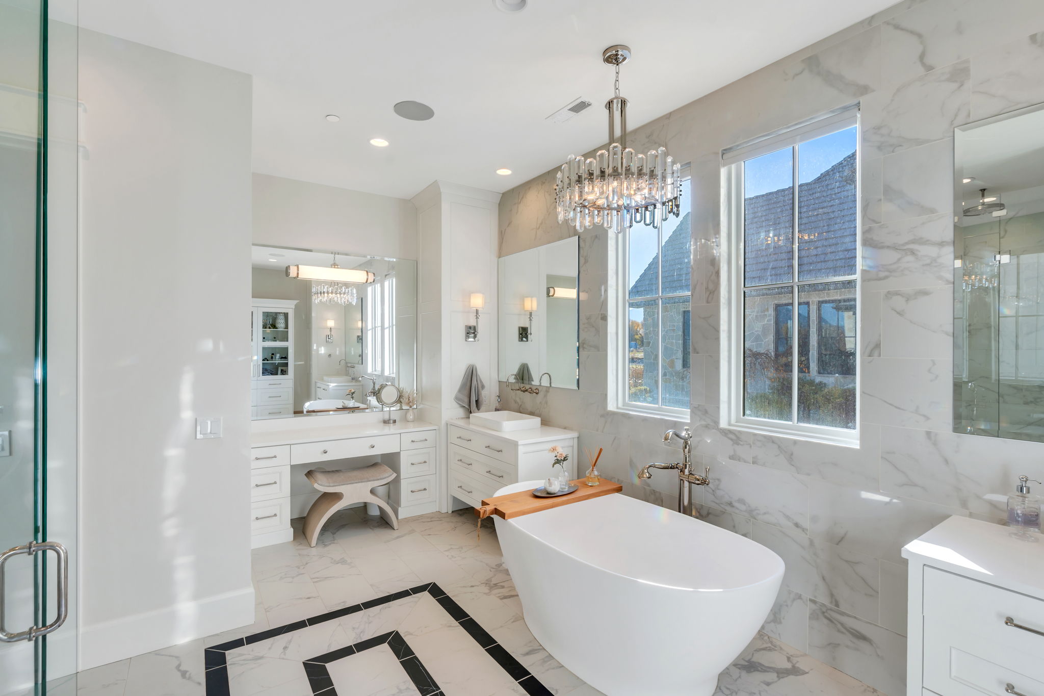 Full bathroom featuring light marble finish flooring, vanity, a marble finish shower, a soaking tub, and a chandelier
