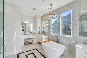 Full bathroom featuring light marble finish flooring, vanity, a marble finish shower, a soaking tub, and a chandelier