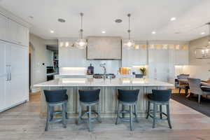 Kitchen featuring glass insert cabinets, hanging light fixtures, white cabinetry, a large island, and light wood-style flooring