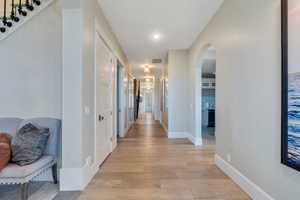 Hallway with light wood-style floors, arched walkways, and recessed lighting