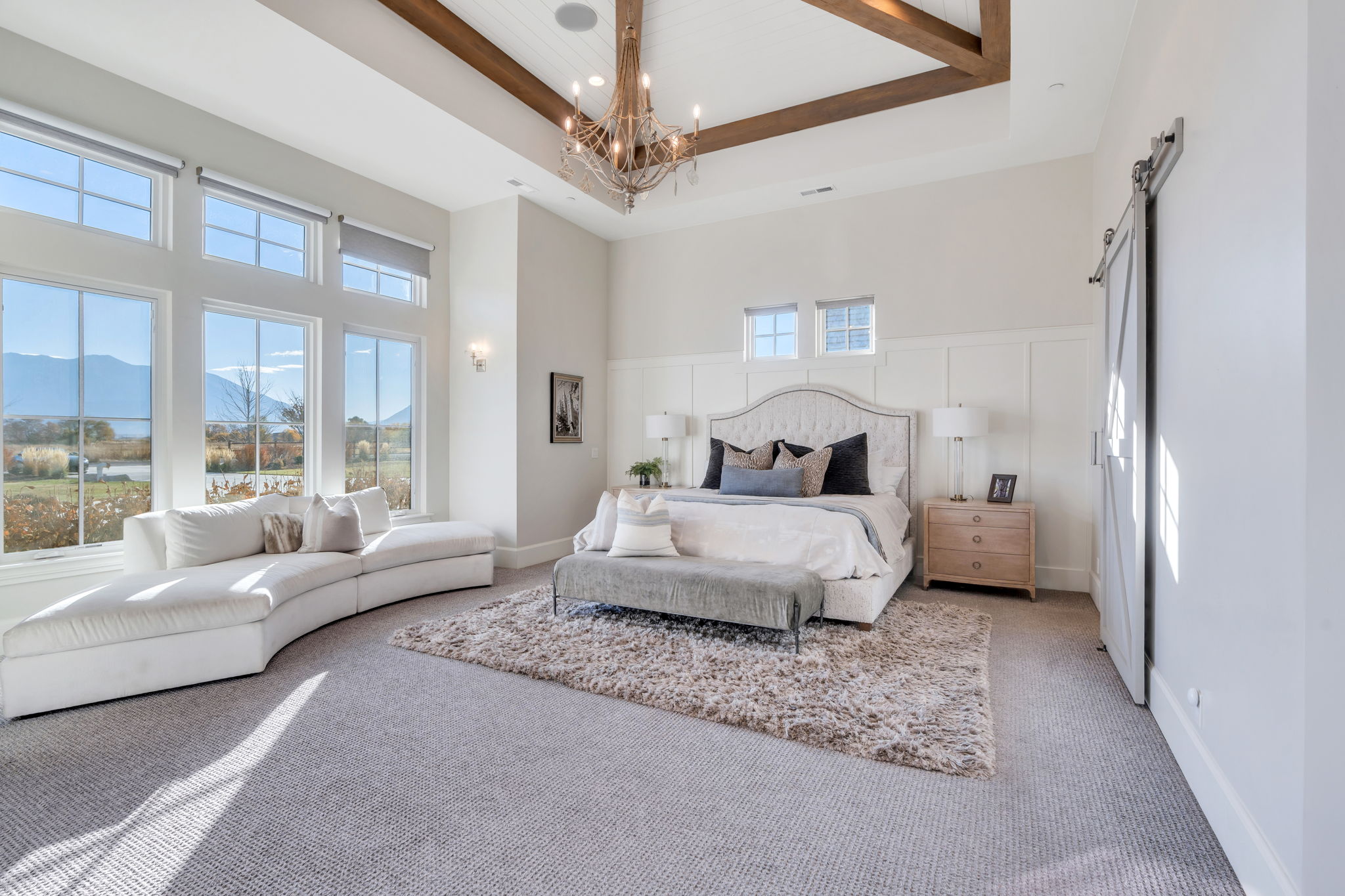 Primary bedroom with a barn door, a raised ceiling, a high ceiling, and a chandelier