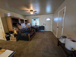 Carpeted living area featuring ceiling fan and baseboards