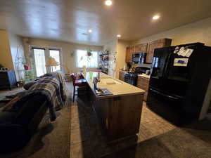 Kitchen with open floor plan, black appliances, light tile patterned flooring, light countertops, and a center island with sink