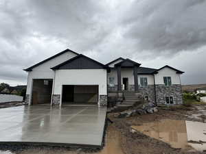 View of front of home with stone siding, a garage, driveway, board and batten siding, and covered porch
