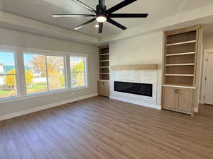 Unfurnished living room featuring a glass covered fireplace, ceiling fan, light wood-style floors, and built in features