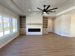 Unfurnished living room featuring a glass covered fireplace, a tray ceiling, light wood-style floors, built in features, and recessed lighting