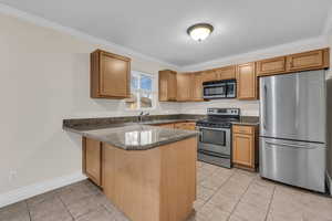 Kitchen with a peninsula, stainless steel appliances, dark stone countertops, light tile patterned floors, and ornamental molding