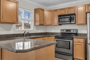 Kitchen featuring stainless steel appliances, a peninsula, crown molding, dark stone countertops, and light tile patterned flooring
