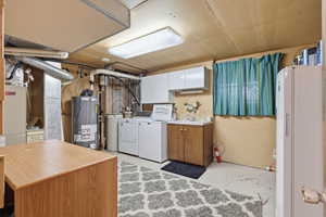 Washroom featuring separate washer and dryer, concrete flooring, water heater, and cabinet space
