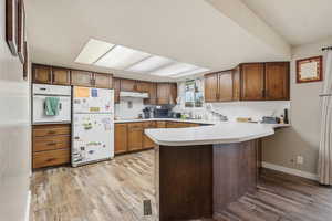 Kitchen with light countertops, white appliances, light wood-style flooring, brown cabinetry, and a peninsula