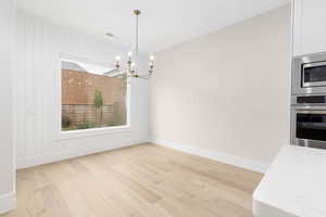 Unfurnished dining area with light wood-style flooring, a chandelier, and wooden walls