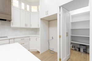 Kitchen featuring light wood finished floors, white cabinetry, backsplash, and glass insert cabinets