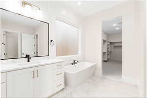 Bathroom featuring a walk in closet, vanity, recessed lighting, a freestanding bath, and light marble finish flooring