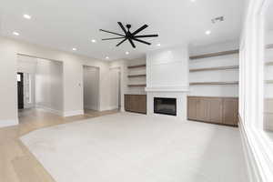 Unfurnished living room featuring a tile fireplace, recessed lighting, light wood finished floors, ceiling fan, and built in features