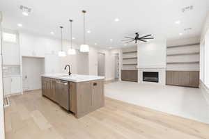 Kitchen featuring open floor plan, pendant lighting, light wood-type flooring, a ceiling fan, and light stone counters