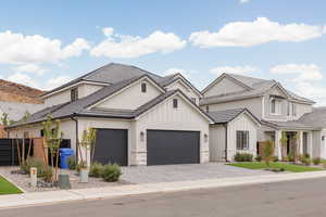 Modern farmhouse featuring decorative driveway, stone siding, an attached garage, a tiled roof, and board and batten siding