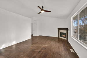 Unfurnished living room with lofted ceiling, dark wood-style flooring, a warm lit fireplace, and a ceiling fan
