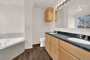 Full bath featuring double vanity, a garden tub, and dark wood finished floors