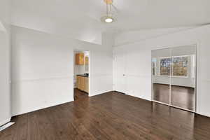 Unfurnished bedroom with a closet, dark wood-type flooring, lofted ceiling, and ensuite bathroom