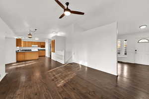 Unfurnished living room featuring vaulted ceiling, dark wood-style flooring, and ceiling fan