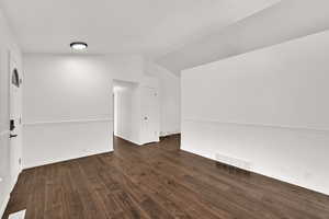 Empty room with vaulted ceiling and dark wood-type flooring
