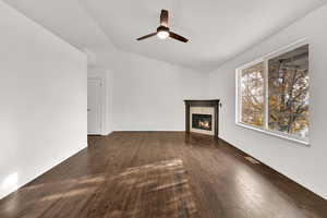Unfurnished living room with lofted ceiling, dark wood-style flooring, a premium fireplace, and ceiling fan