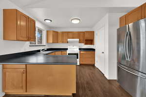 Kitchen with freestanding refrigerator, a peninsula, white electric stove, dark wood-style floors, and under cabinet range hood