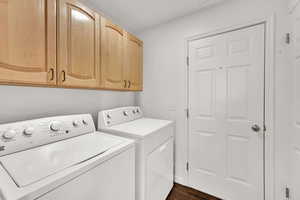 Washroom featuring dark wood-style flooring, washer and clothes dryer, and cabinet space