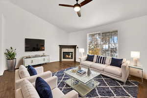 Living room with dark wood finished floors, vaulted ceiling, a glass covered fireplace, and a ceiling fan