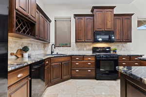 Kitchen with dark stone countertops, black appliances, dark brown cabinetry, and backsplash