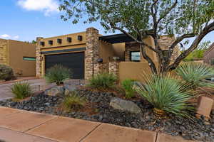 Southwest-style home featuring stucco siding, driveway, a garage, and stone siding