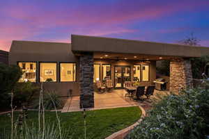 Back of property at dusk with a ceiling fan, stucco siding, a patio, stone siding, and a yard
