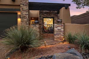 Entrance to property with stone siding, stucco siding, a garage, and a patio