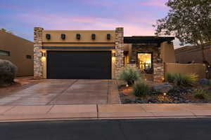 Pueblo-style house with concrete driveway, stucco siding, stone siding, and an attached garage