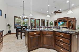 Kitchen with dark brown cabinets, hanging light fixtures, dark stone countertops, a center island with sink, and recessed lighting