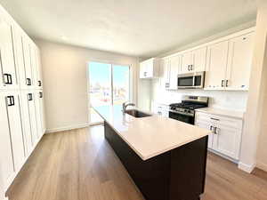 Kitchen featuring appliances with stainless steel finishes, white cabinets, a kitchen island with sink, light wood-style flooring, and recessed lighting