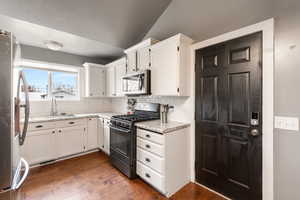 Kitchen with stainless steel appliances, white cabinets, backsplash, dark wood-type flooring, and lofted ceiling
