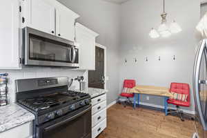 Kitchen featuring stainless steel appliances, white cabinetry, light stone countertops, light wood finished floors, and a towering ceiling