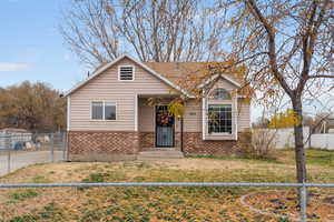 Bungalow-style home featuring a fenced front yard, brick siding, and roof with shingles