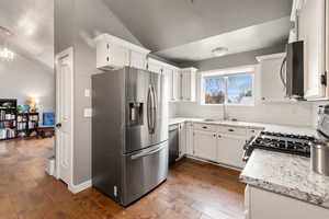 Kitchen featuring appliances with stainless steel finishes, lofted ceiling, dark wood finished floors, backsplash, and white cabinetry